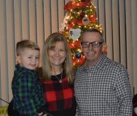 Boy held by woman, next to man, in front of a Christmas tree.