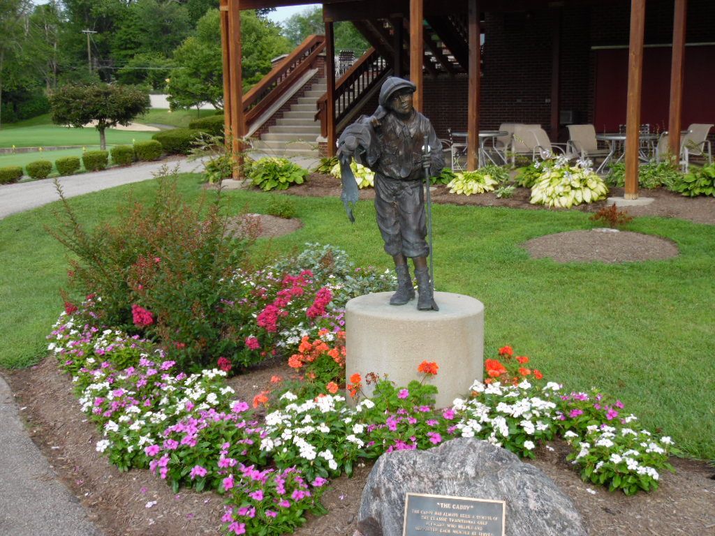 Bronze statue of a golfer in front of a wooden building and flowerbed.