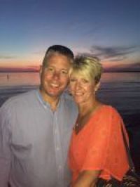 Couple smiling on beach at sunset. Man in blue shirt, woman in orange top.