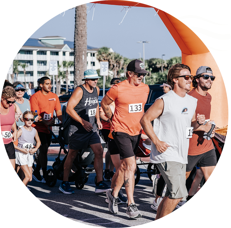 Runners in numbered bibs starting a road race near an orange arch on a sunny day
