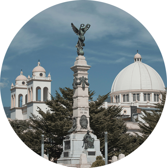 Church towers and a white dome behind a stone monument with an angel statue under a cloudy sky