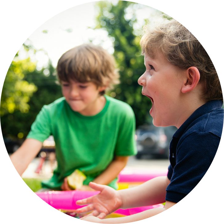 Two children playing with colorful toys outdoors, one laughing in the foreground