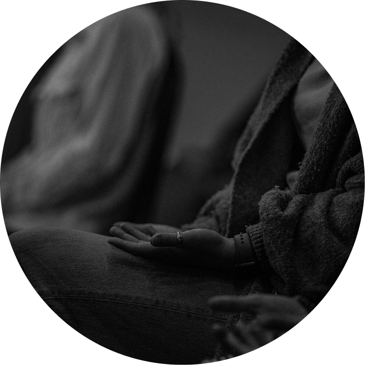 A black-and-white close-up of a person’s hand resting on their lap in a dim setting