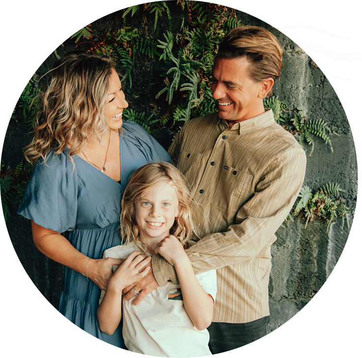 Three smiling people pose together in front of leafy greenery.