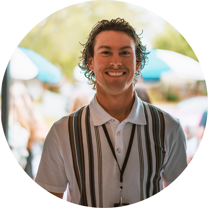 Smiling man in a striped shirt standing outdoors at a bright event