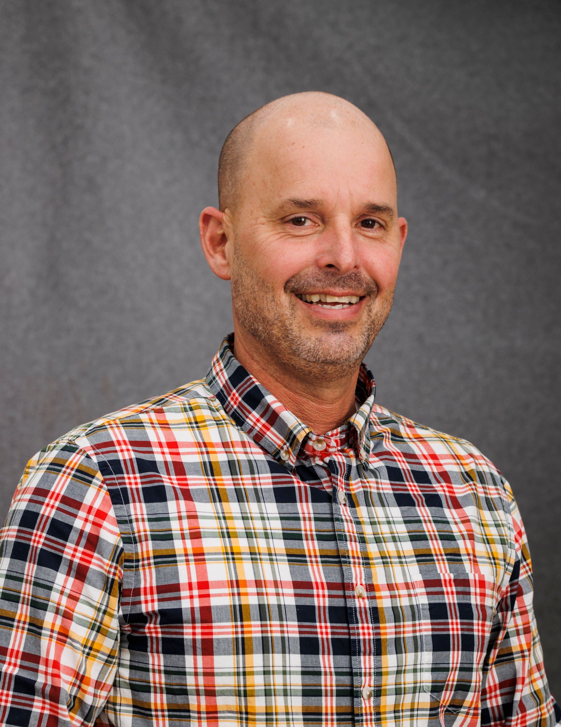 A man wearing a plaid shirt is smiling for the camera.