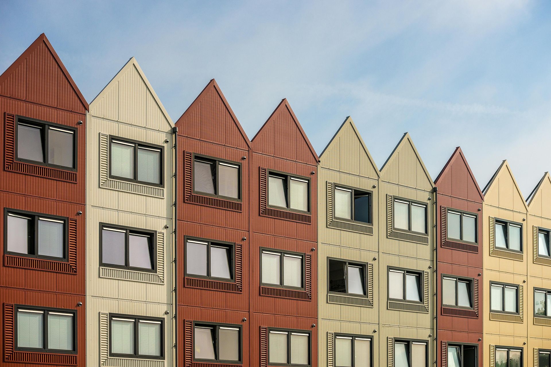 A row of residential buildings with pointed gables and a repeating pattern of tan and reddish-brown corrugated metal walls.