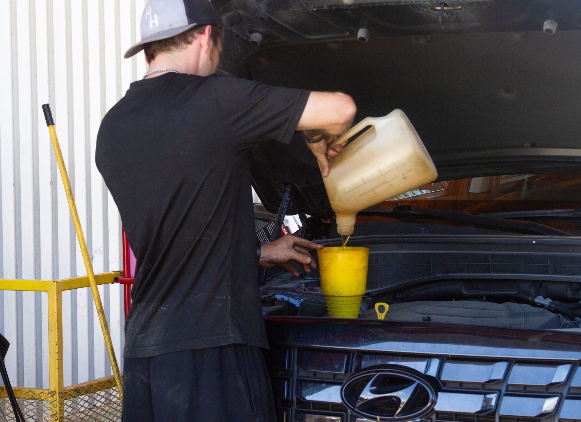 Man in black shirt pouring fluid into a car, possibly oil, with a funnel.