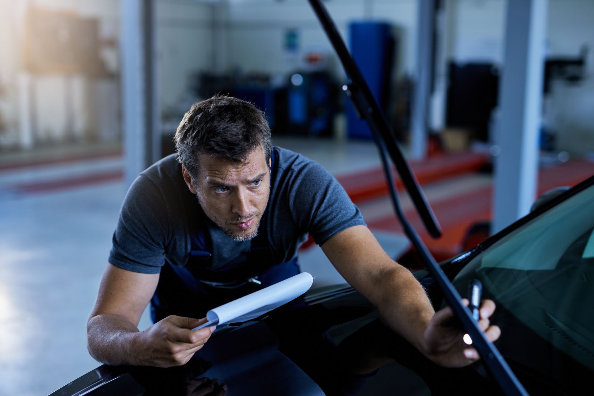 A man is checking the wiper blades of a car in a garage.