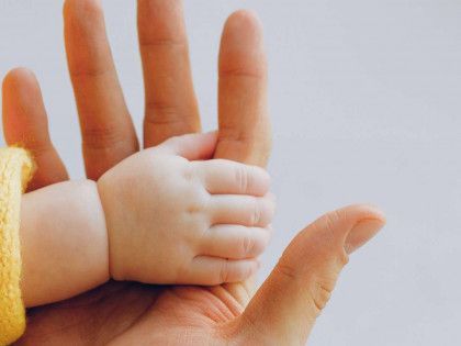Adult hand holding a baby's hand and fingers in close-up