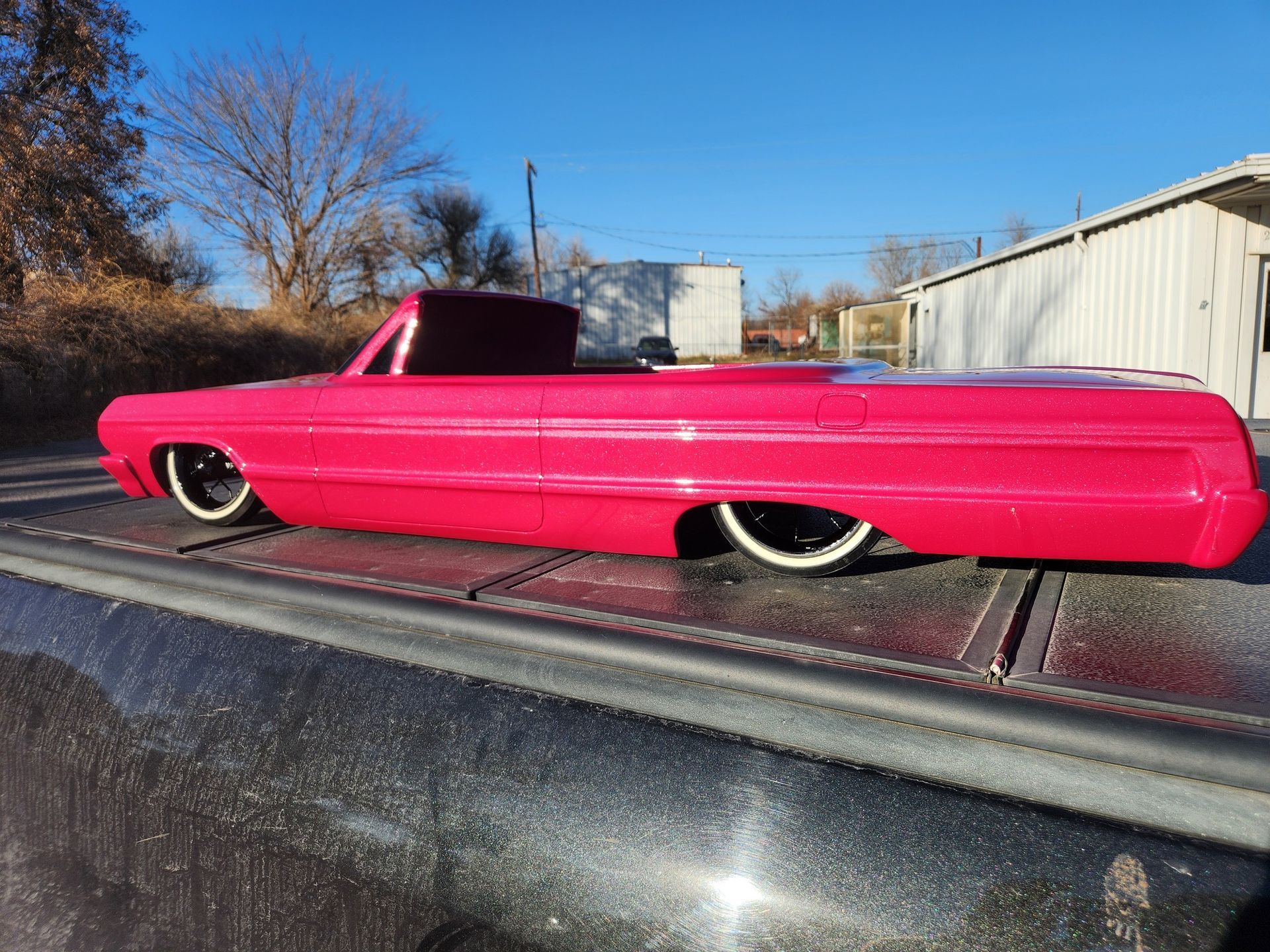 Bright pink lowrider car with whitewall tires on a trailer outdoors under a clear blue sky