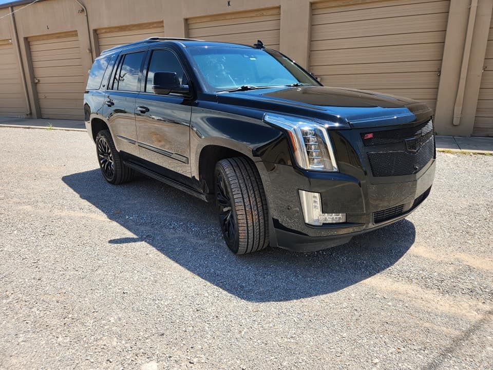 Black Cadillac SUV parked on a sunny driveway in front of beige garage doors