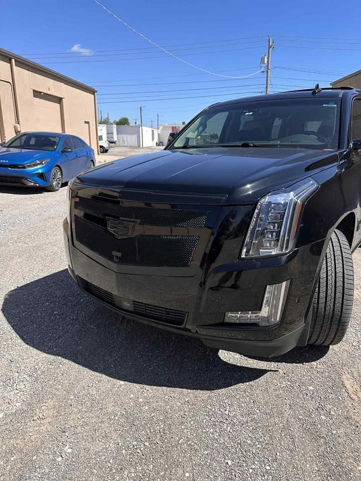 Black SUV parked in an industrial lot, with a blue car and warehouse in the background.