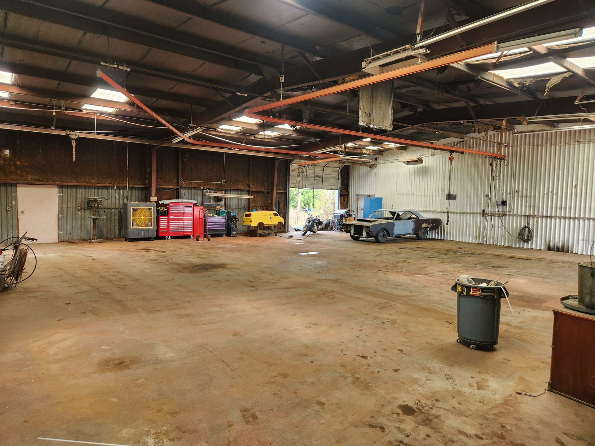 Empty industrial warehouse with concrete floor, corrugated metal walls, and a few carts and bins along the back wall