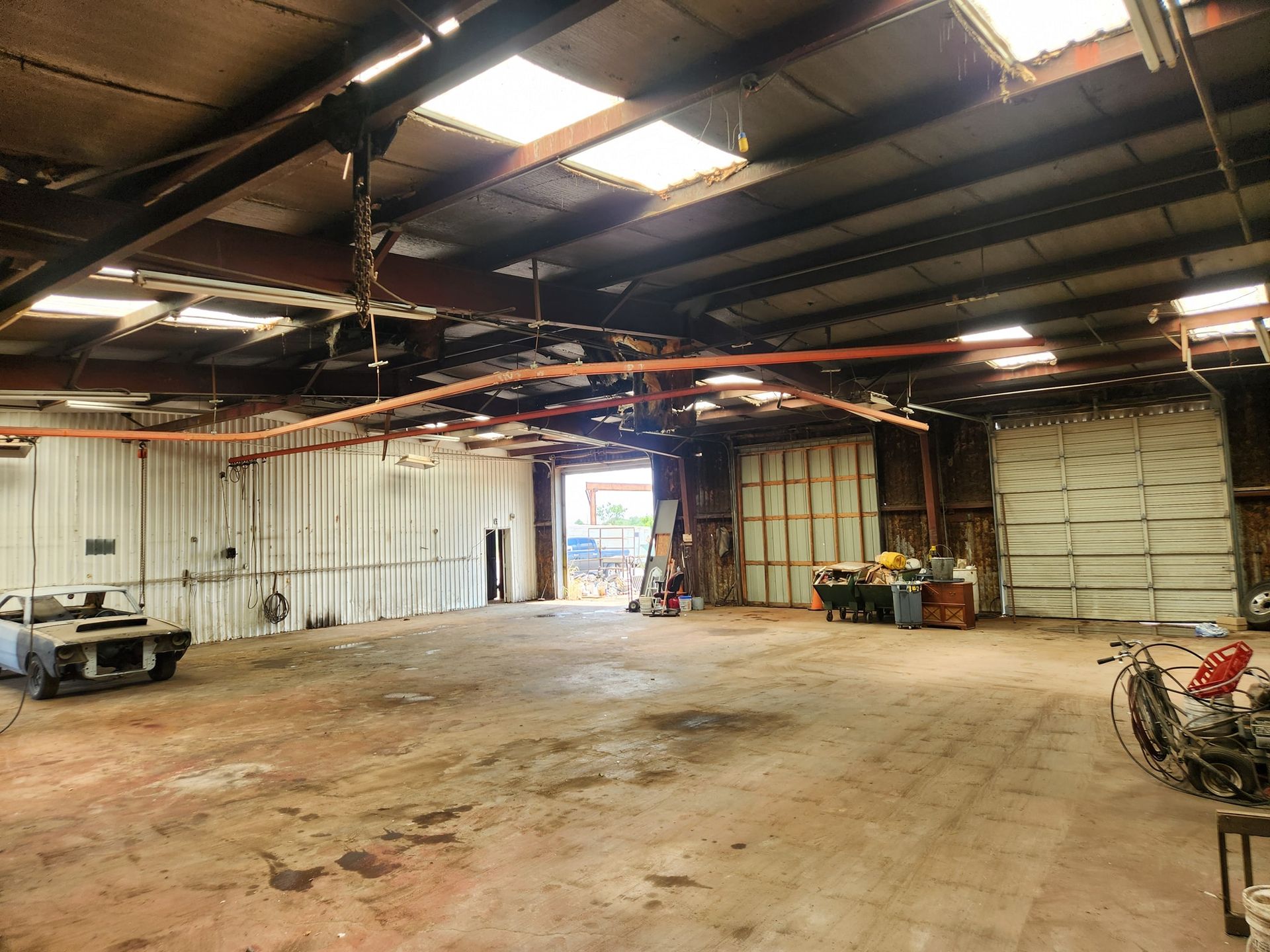 Empty industrial warehouse with a concrete floor, open garage door, and skylights in the ceiling
