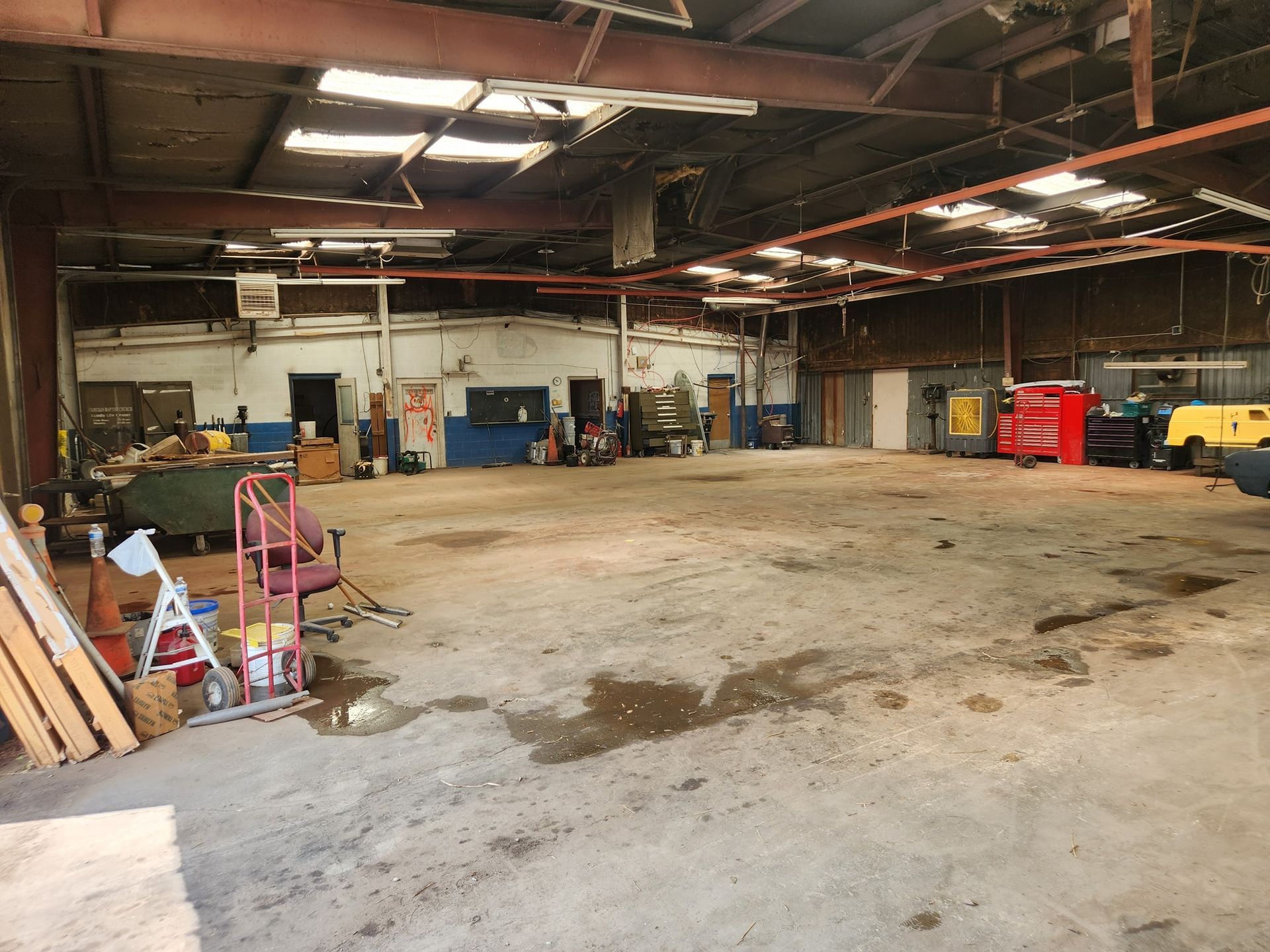 Empty industrial warehouse with concrete floor, exposed beams, and scattered tools along the walls