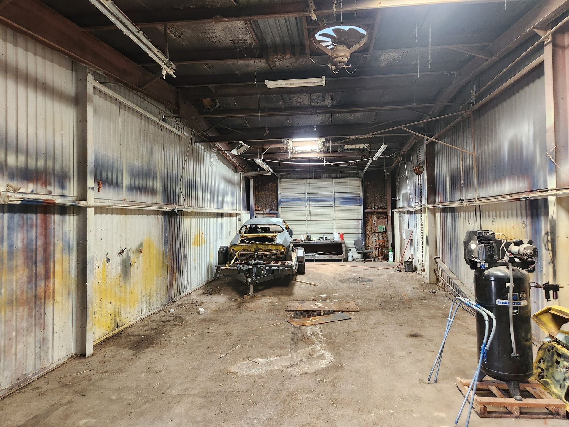 Abandoned industrial garage with rusted cars, debris, and machinery under a dim ceiling.