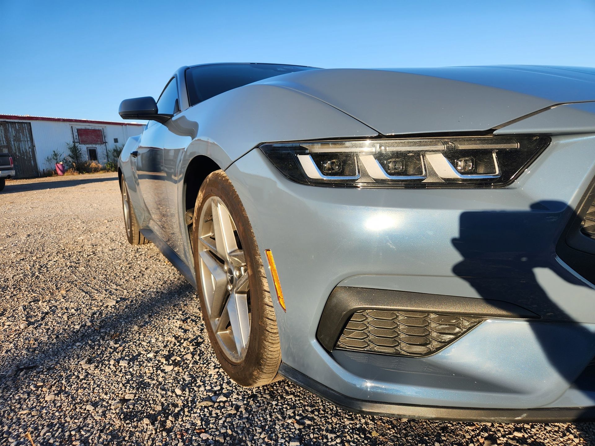 Silver sports car parked on gravel, front-left close-up in bright sunlight.