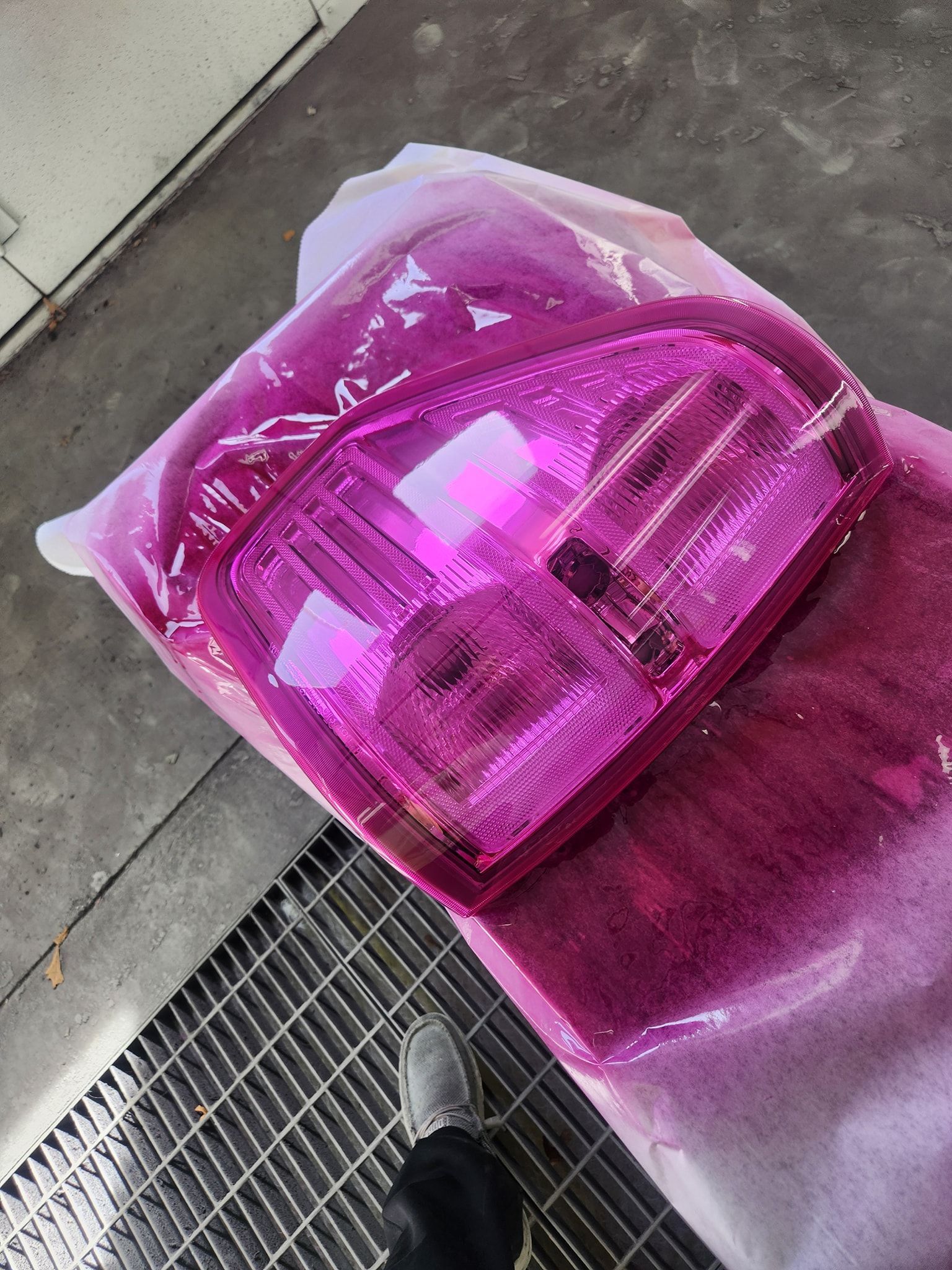 Bright pink transparent tote bag on a sidewalk, viewed from above beside a shoe and drain grate