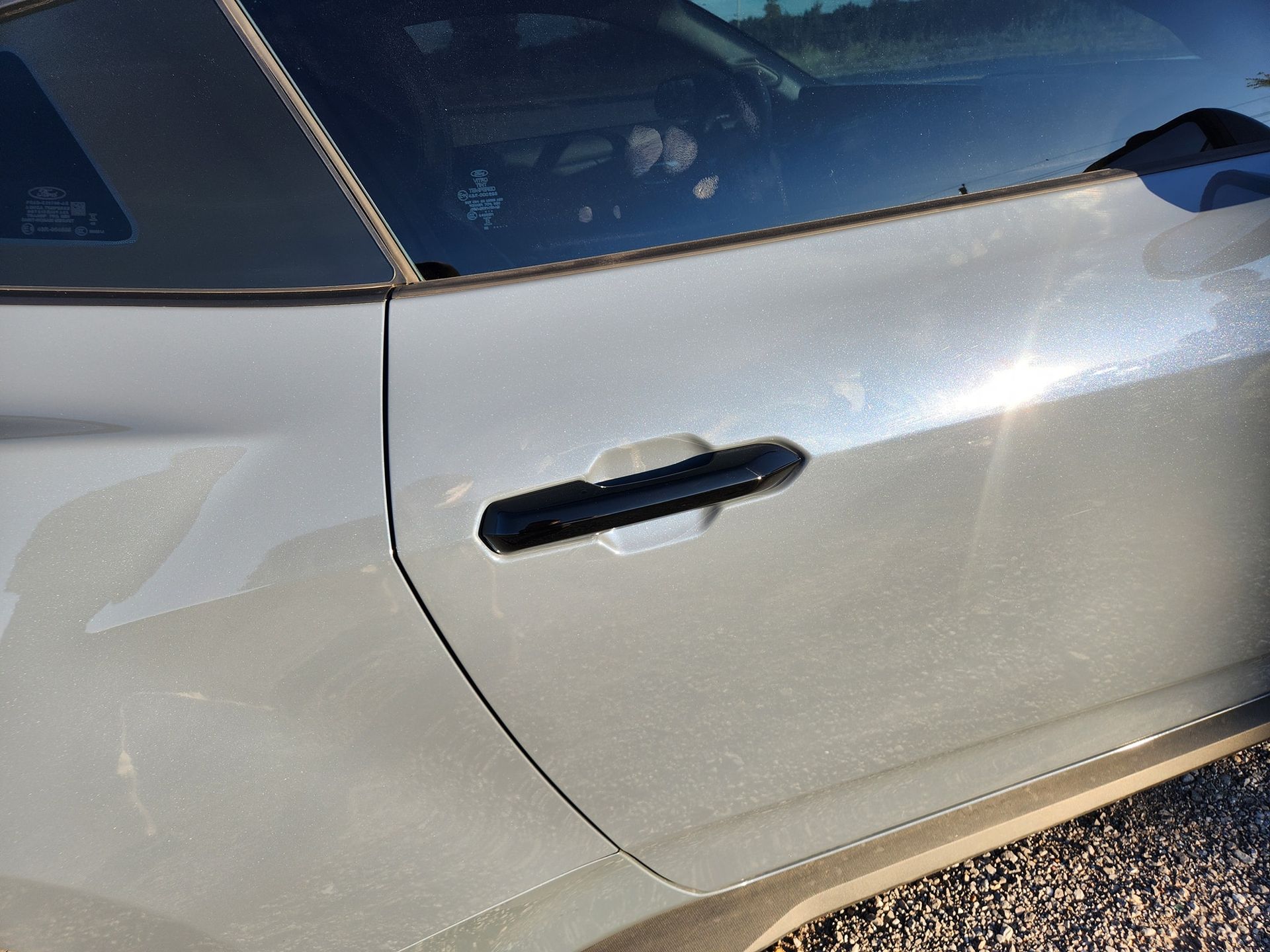 Close-up of a silver car door with a black handle and visible dirt speckles.