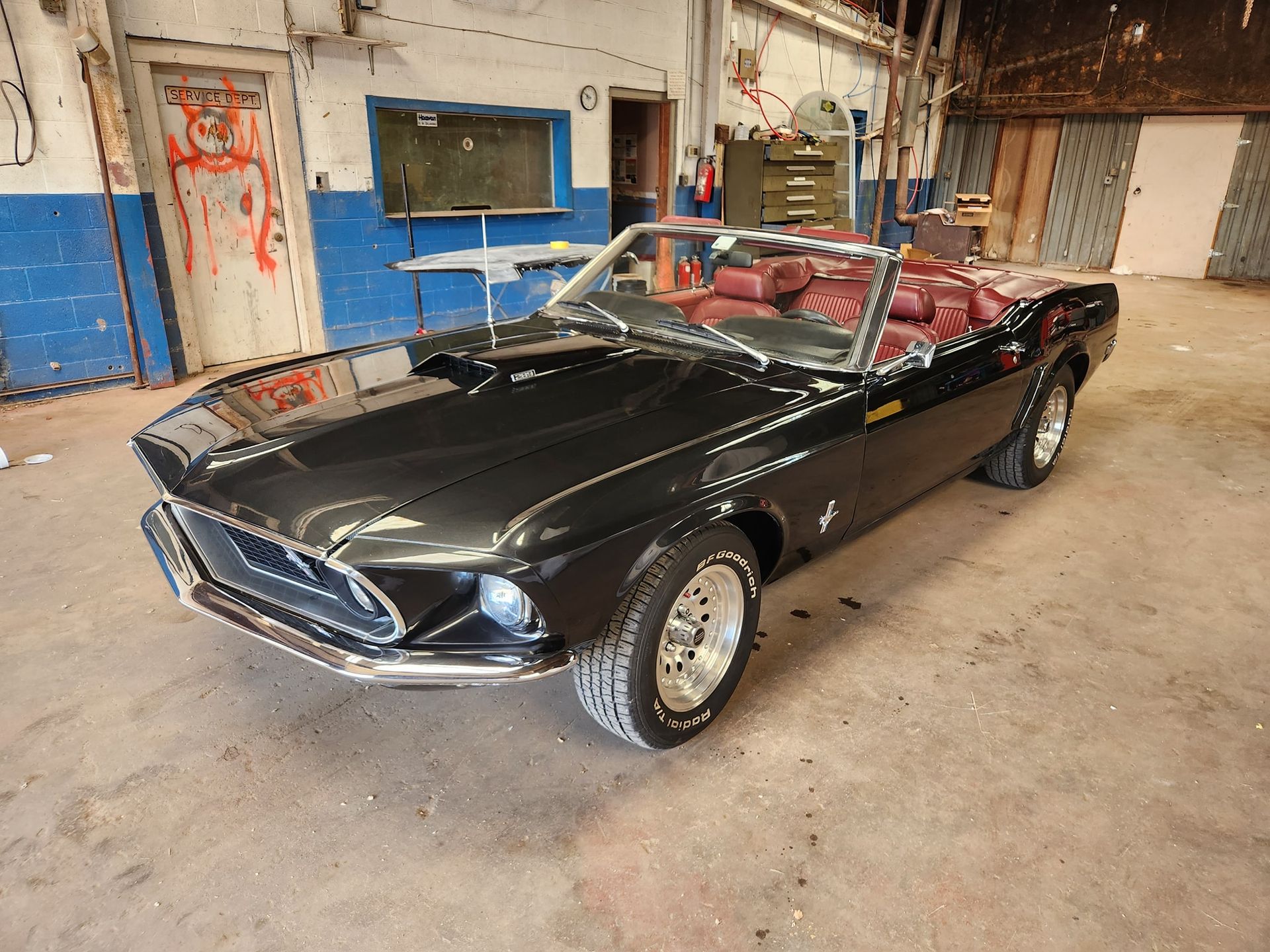 Black classic convertible with red interior parked in an industrial garage