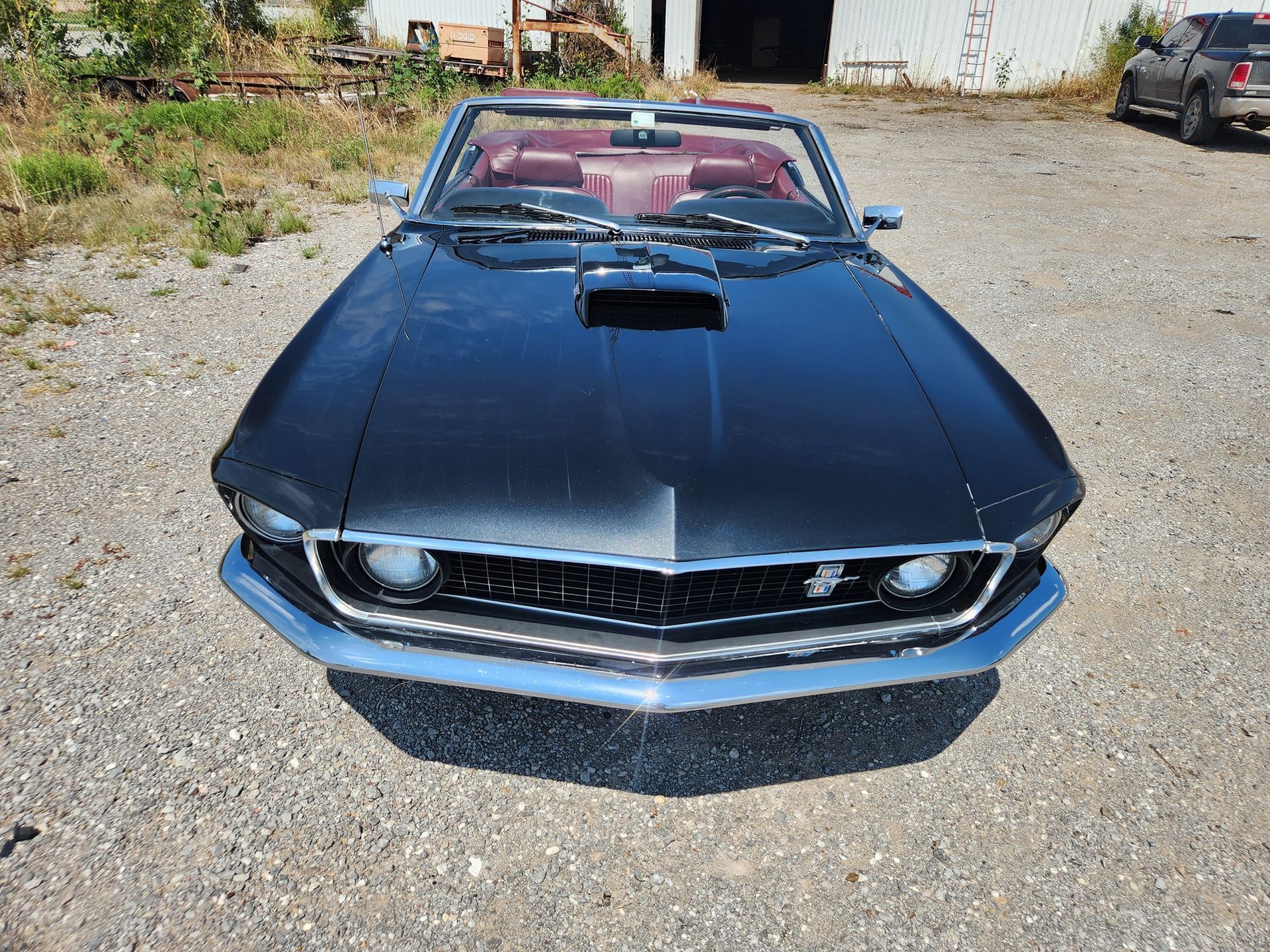 Black classic convertible sports car parked on gravel, front view with red interior.