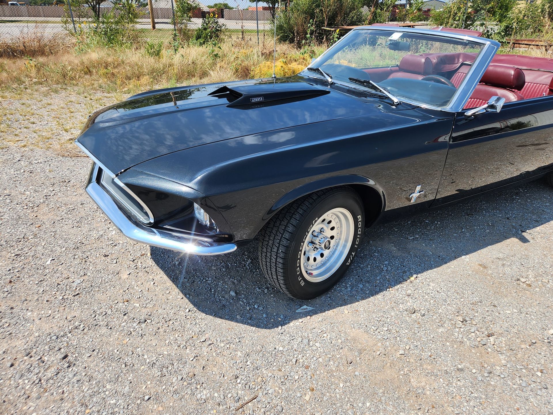 Black classic convertible car with red interior parked on a gravel lot