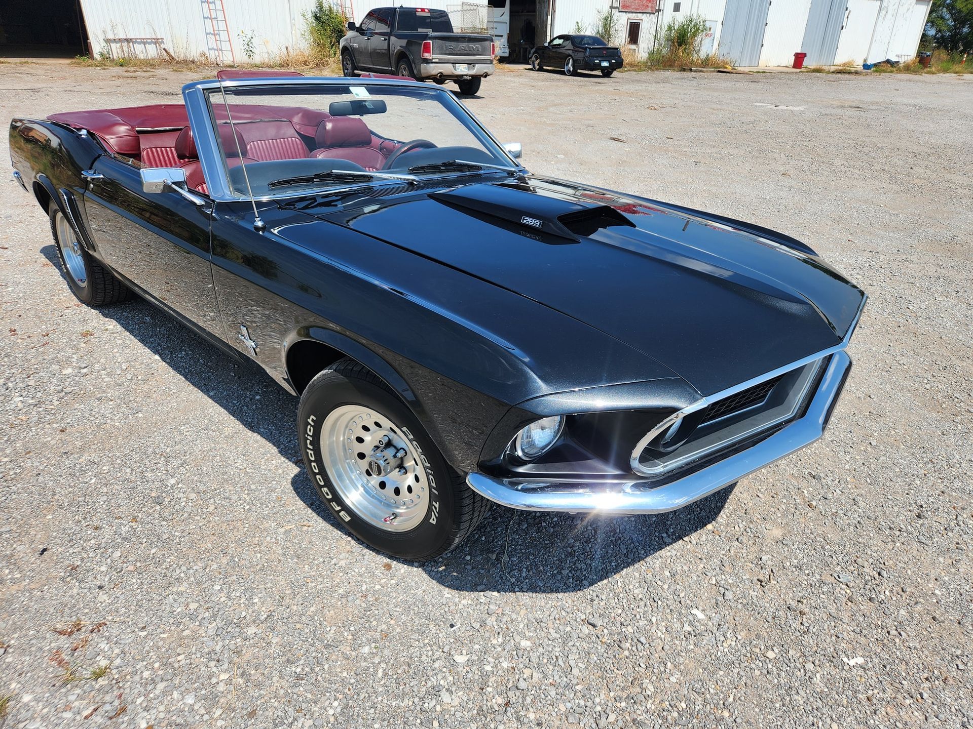 Black vintage convertible parked on gravel, with red interior and chrome trim