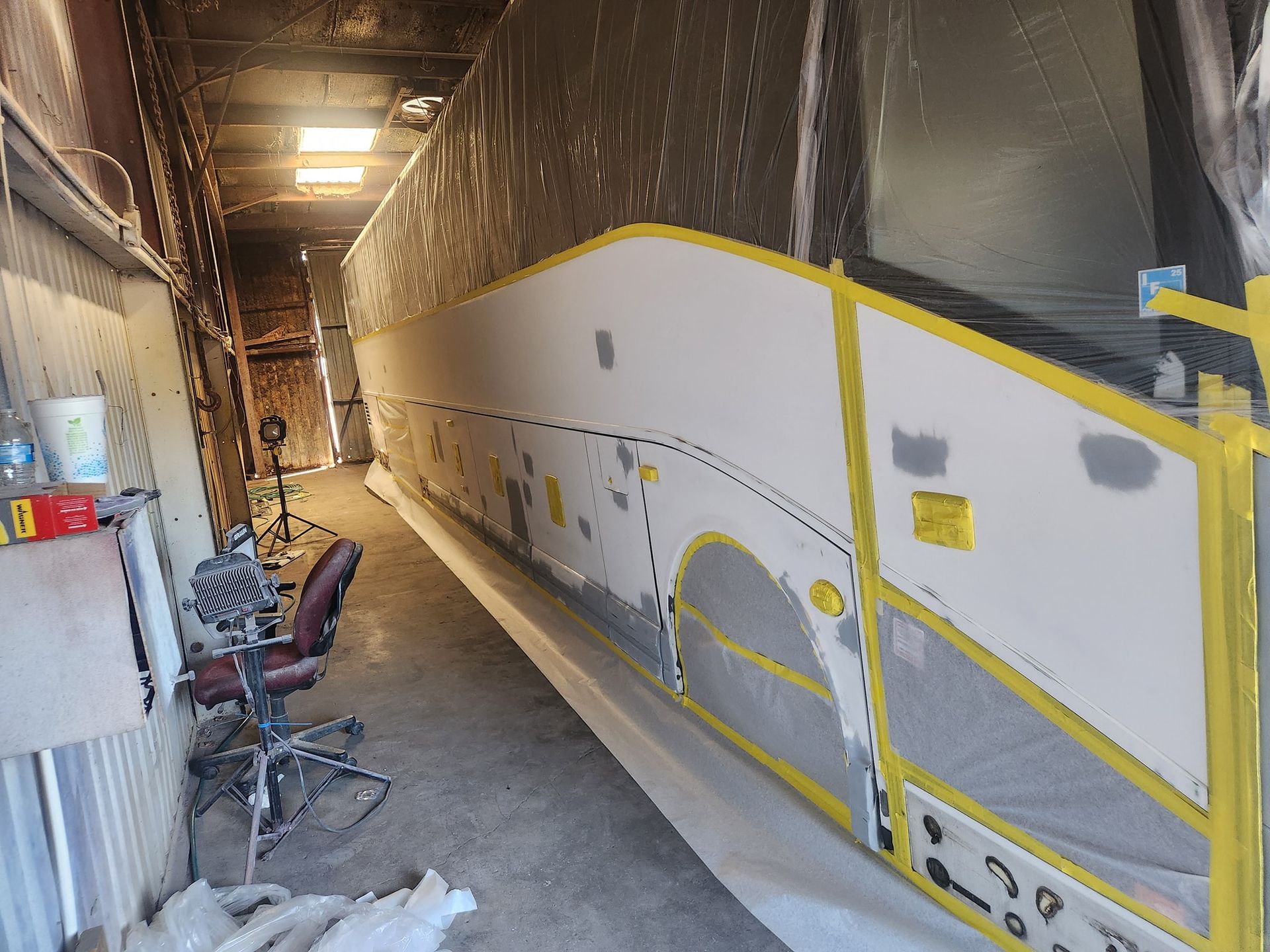 Large bus or trailer interior under construction, with white walls, yellow tape, and work tools along the side.