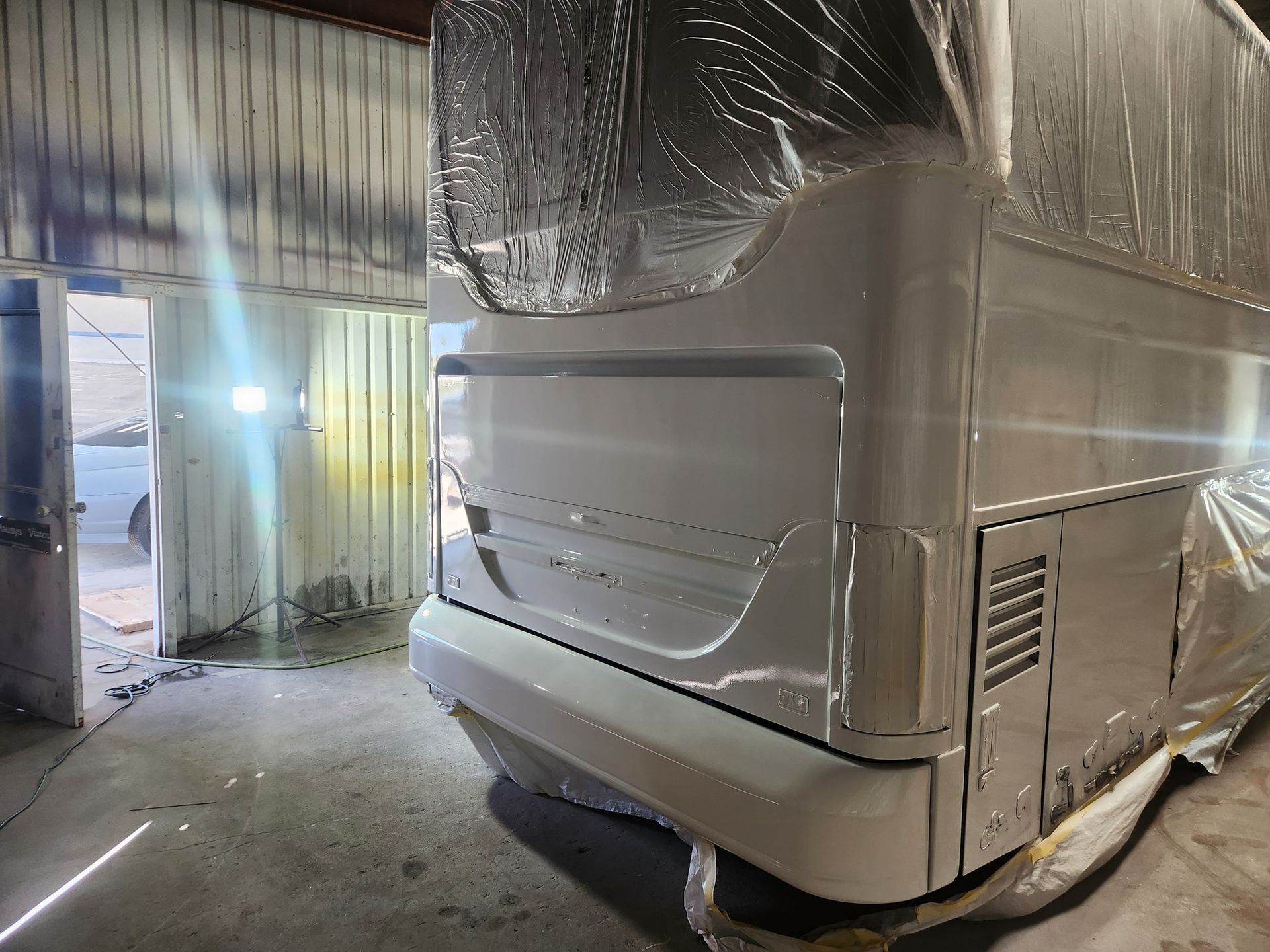 Large white bus in a garage bay, wrapped in plastic and partially covered with protective sheeting
