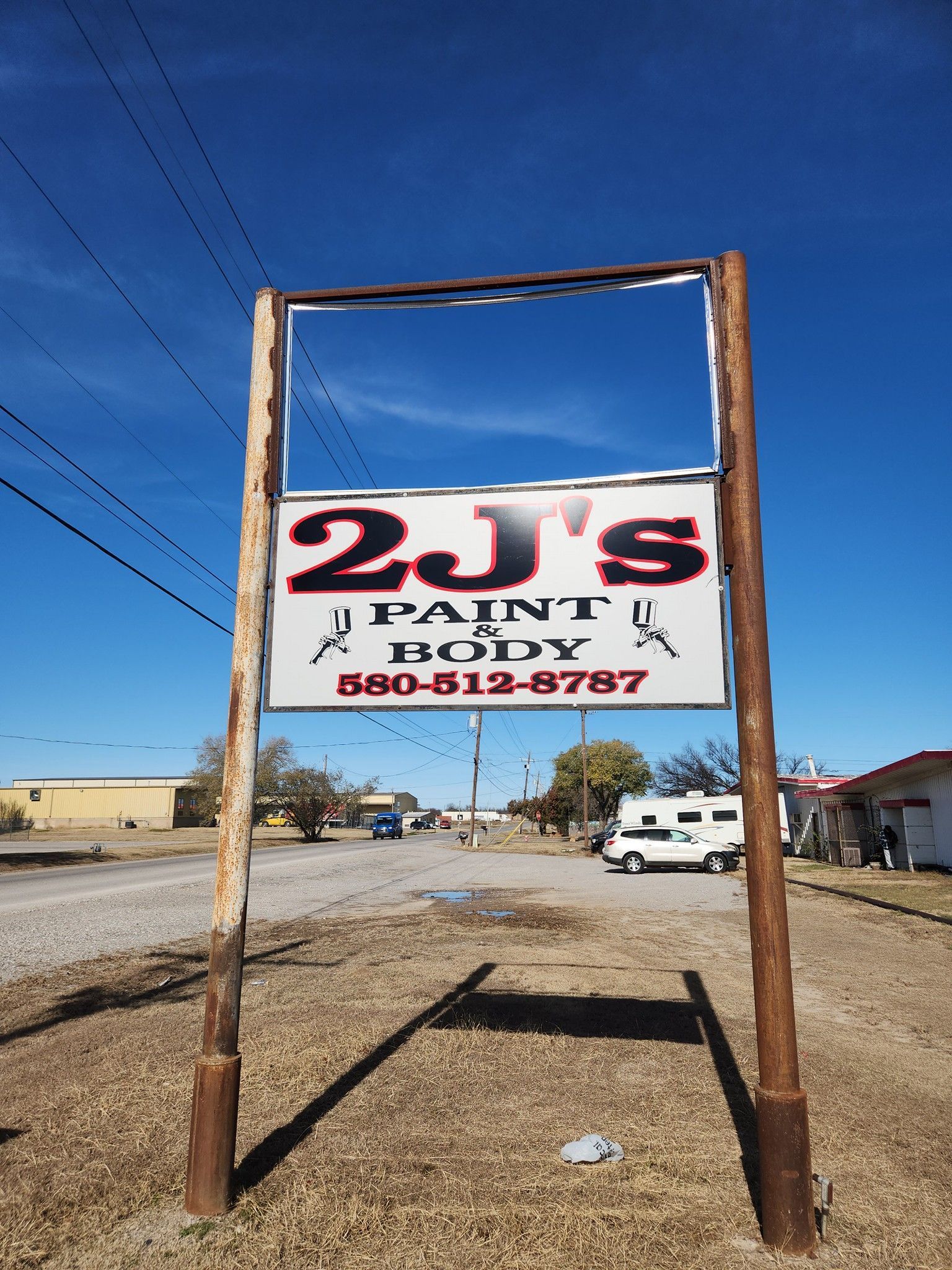 Rusty roadside sign for 2J's Paint & Body under a clear blue sky