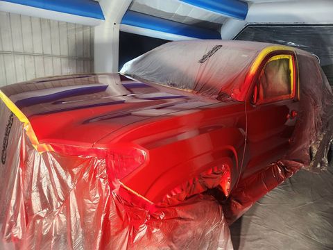 Red car masked for paint in a workshop, covered with plastic and lit by red work light