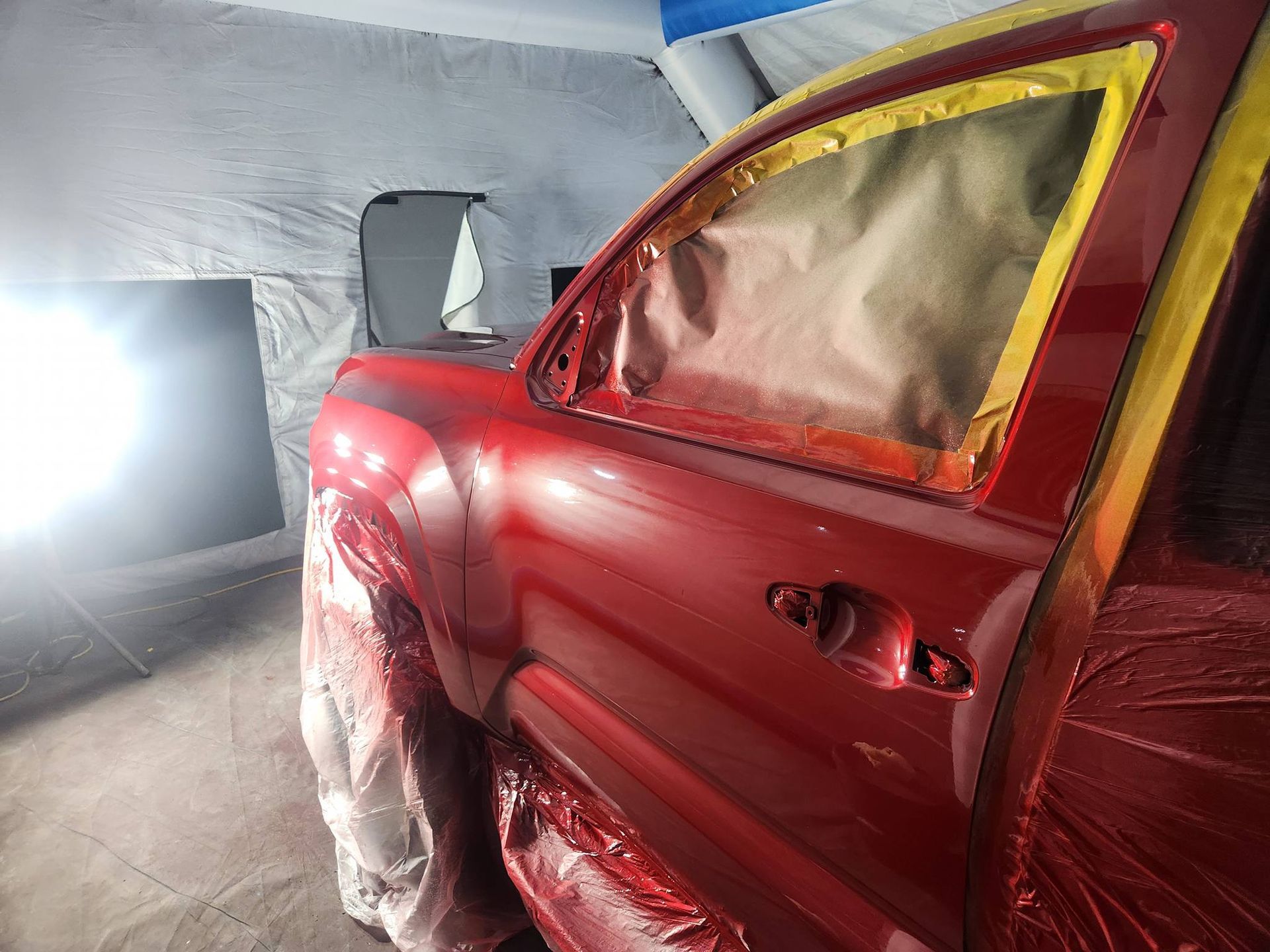 Red car in a body shop, partially masked with plastic for painting or repair