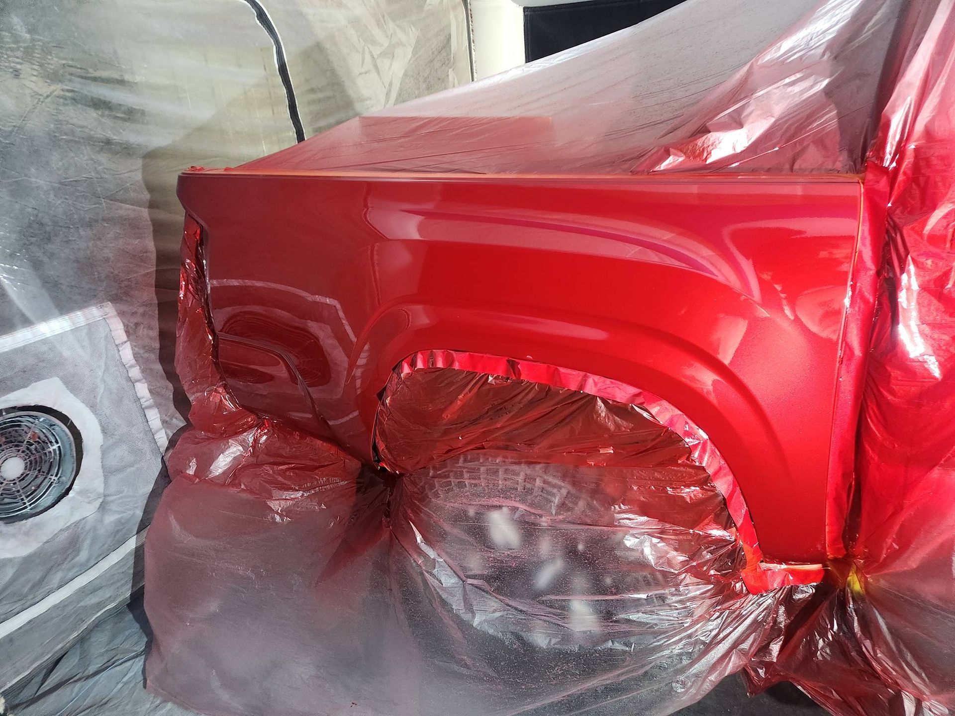 Red car body partially covered in clear plastic wrap during painting or repair