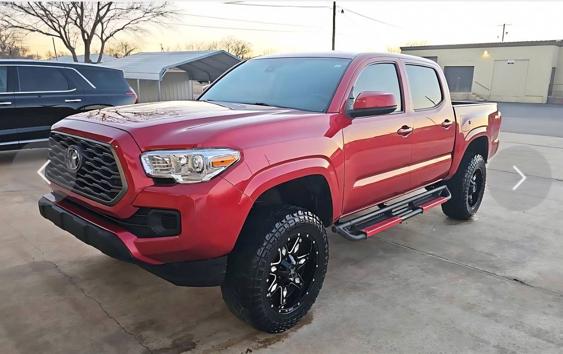 Red pickup truck with black wheels parked outdoors on a concrete lot at sunset