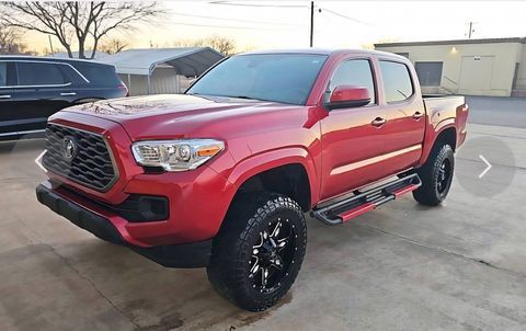 Red pickup truck with black wheels parked outdoors on a concrete lot at sunset