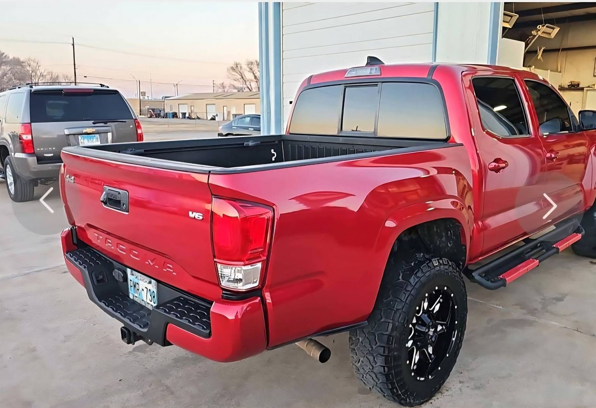 Red pickup truck parked outside a garage, seen from the rear side.
