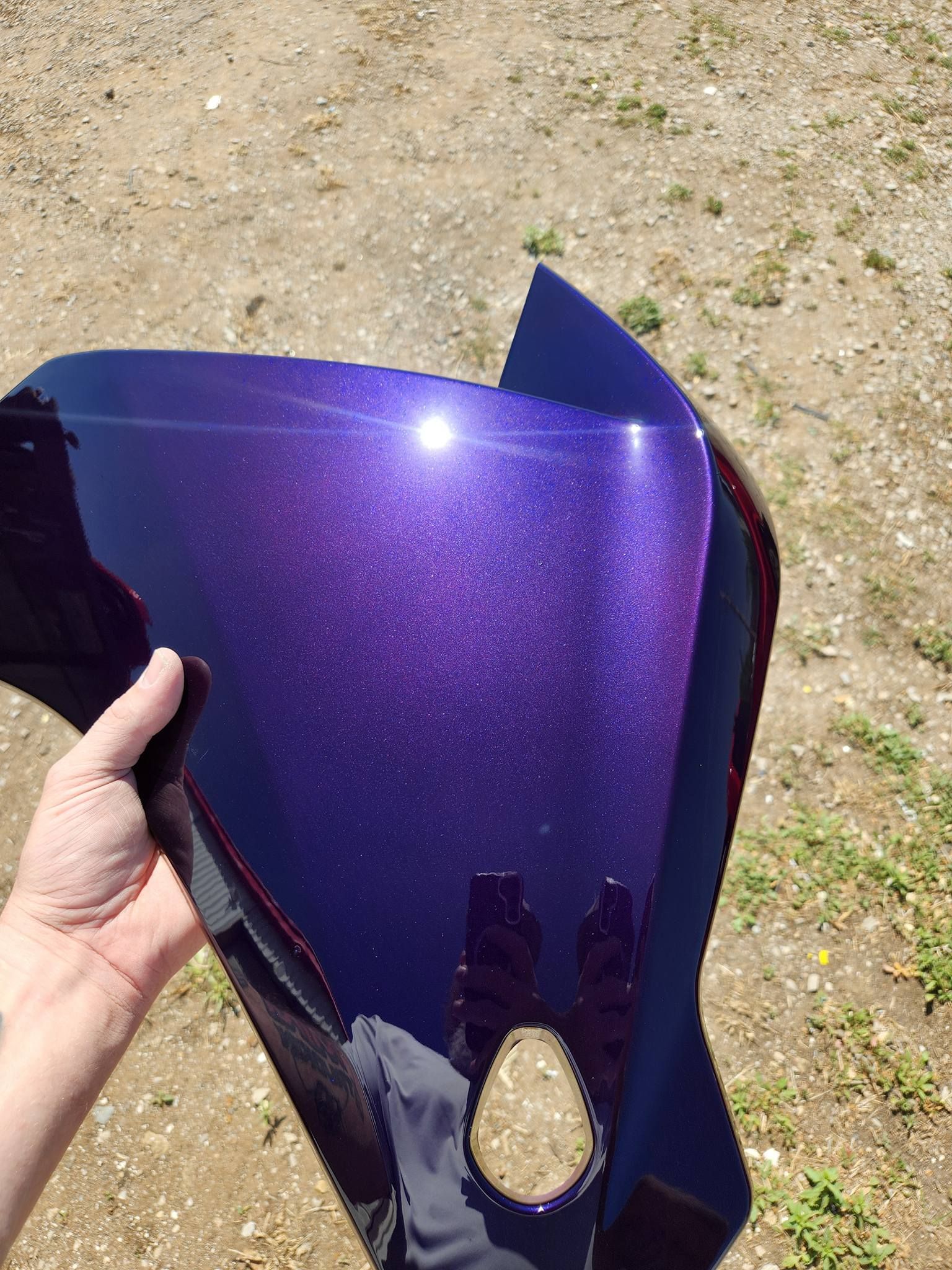 Hand holding a purple glittery motorcycle fairing outdoors on dirt