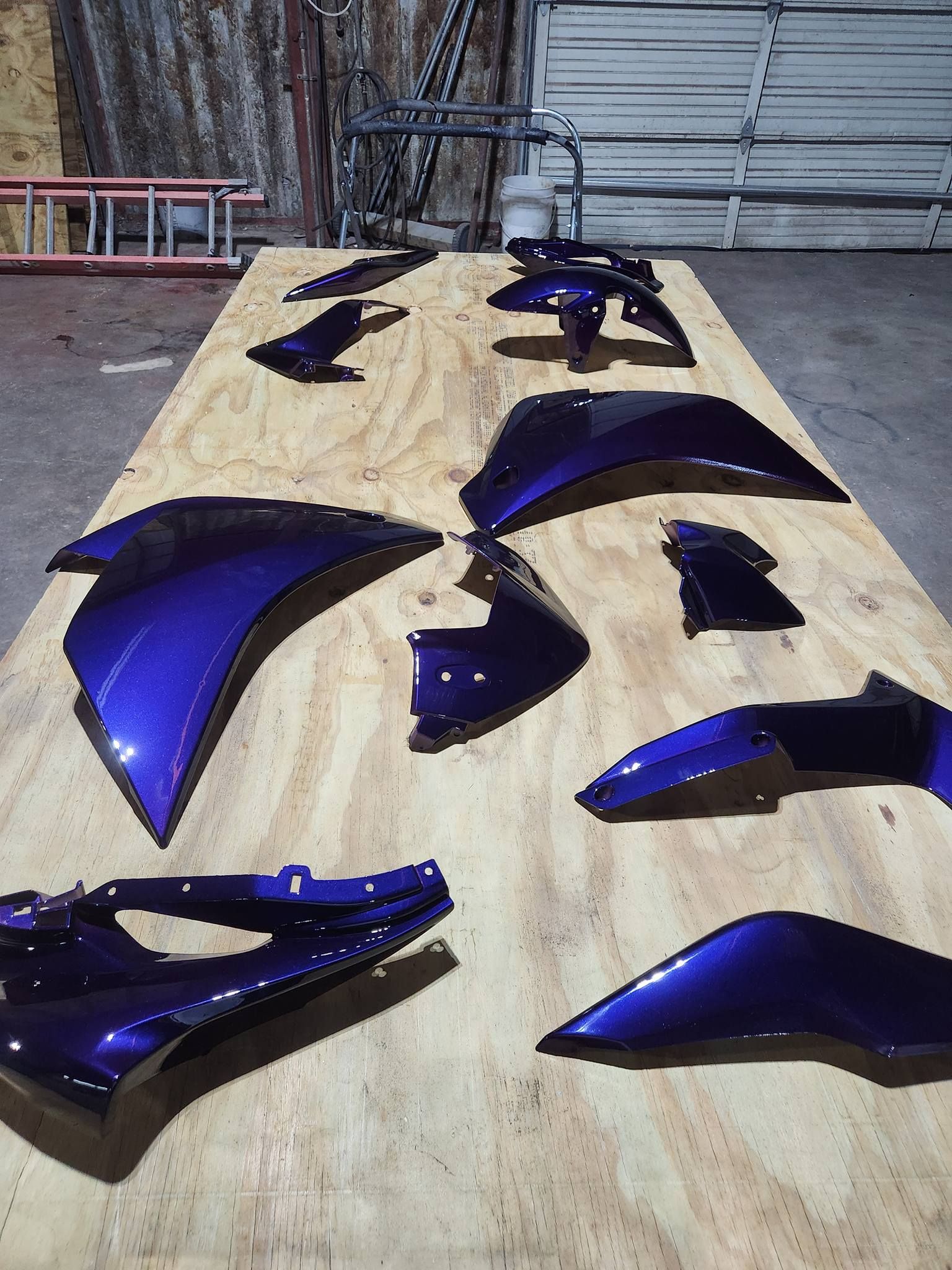 Blue motorcycle fairing pieces laid out on a wooden workbench for assembly or repair
