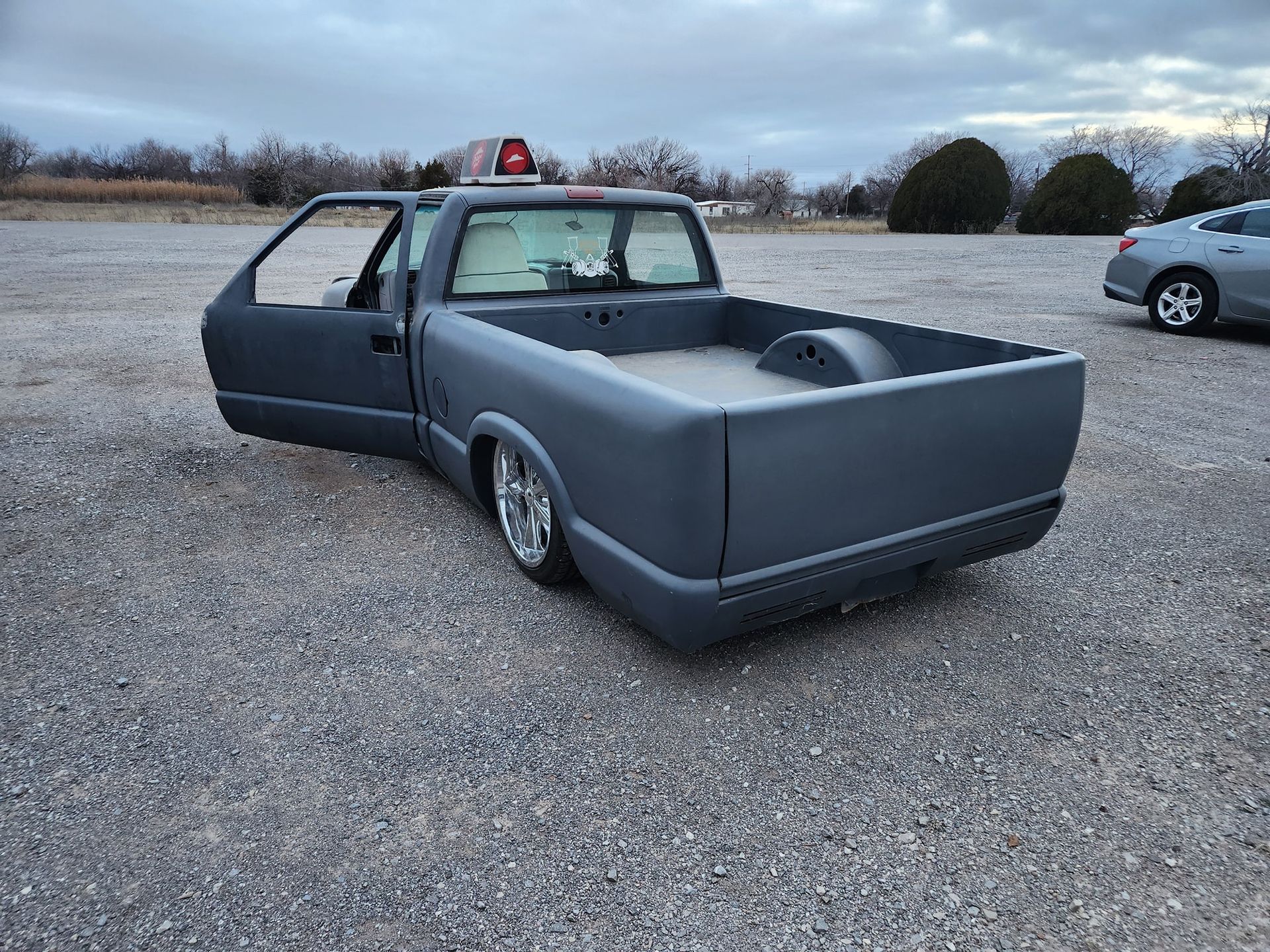Gray custom pickup truck with open driver door parked on a gravel lot at dusk