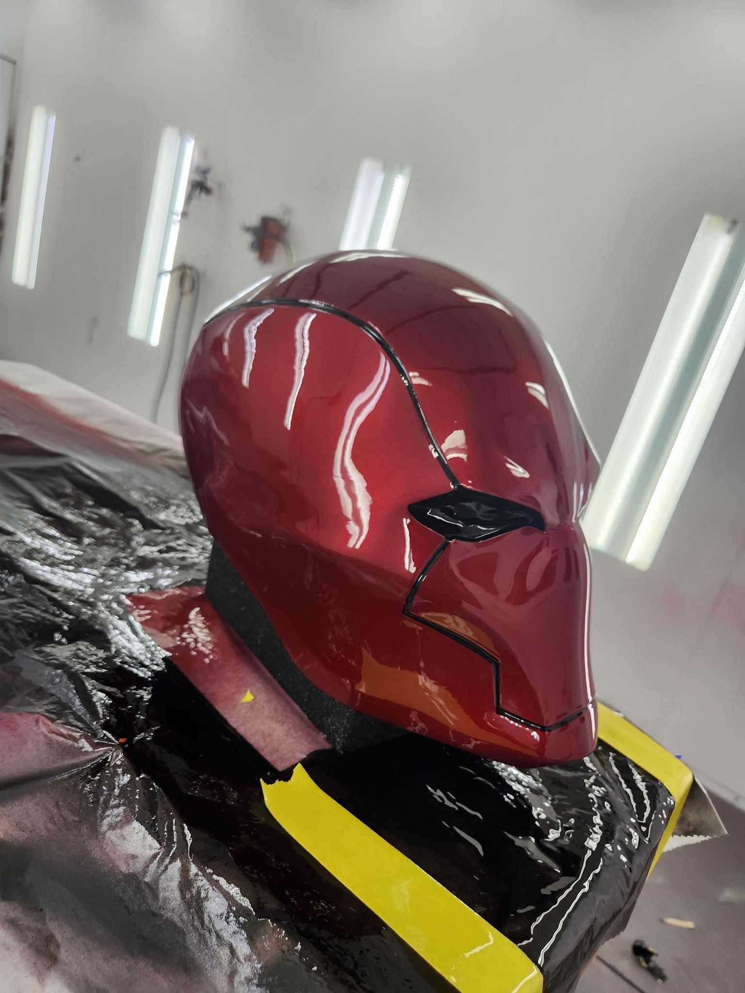 Red Iron Man-style helmet in a workshop, glossy finish with black and yellow accents, under bright lights