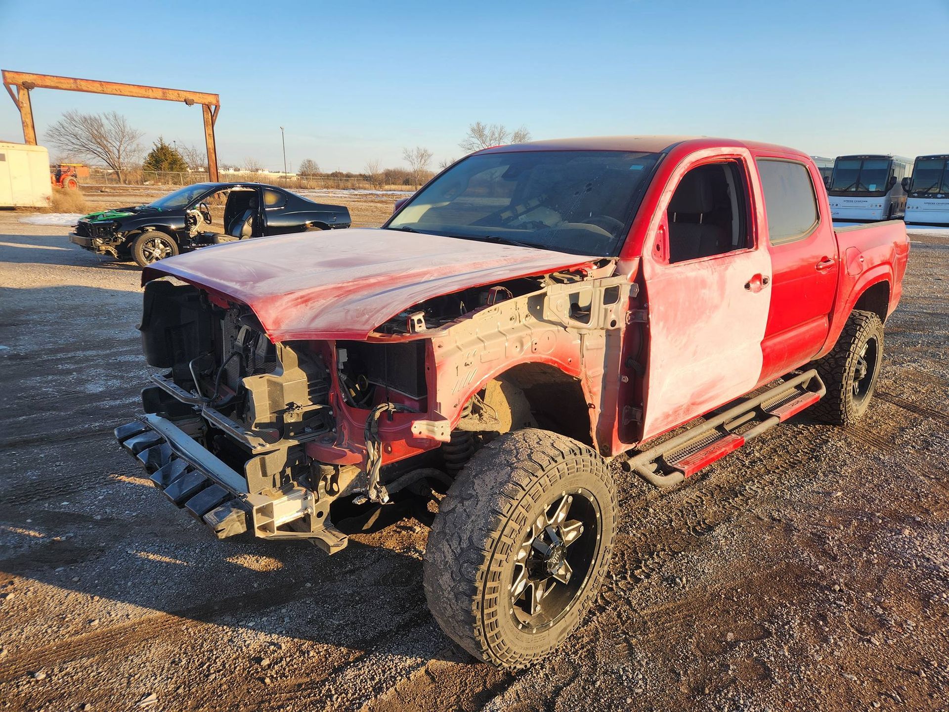 Red pickup truck with a damaged front end parked on a gravel lot at sunset