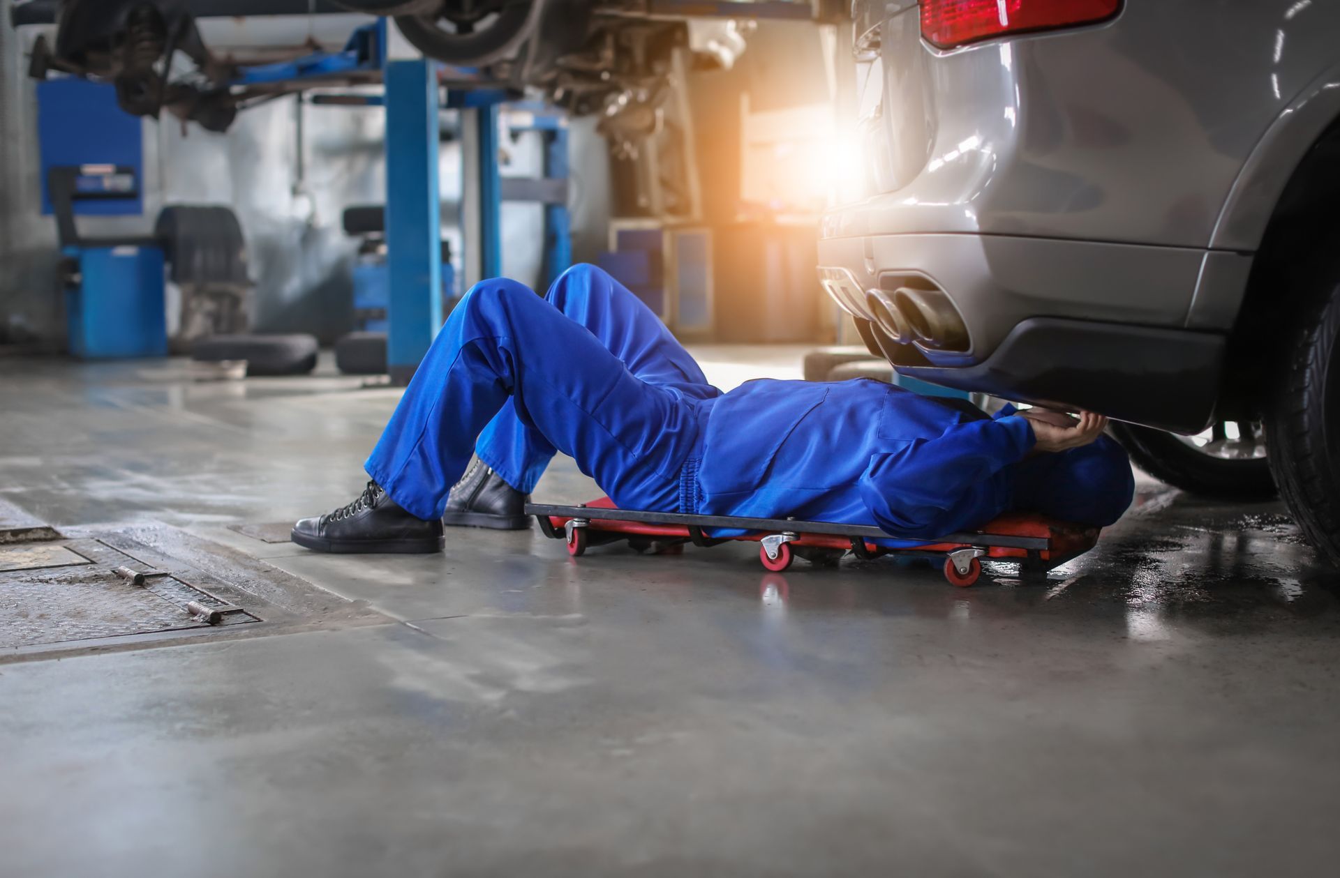 Mechanic lying under a car in a garage, working on the underside with tools nearby. Mechanic lying under a car in a garage, working on the underside with tools nearby.