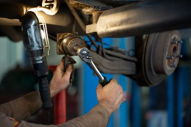 Mechanic tightening a pipe fitting under a vehicle with a wrench in a garage Mechanic tightening a pipe fitting under a vehicle with a wrench in a garage