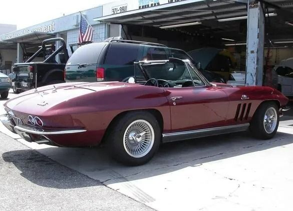 Maroon classic convertible sports car parked outside a garage with the hood open