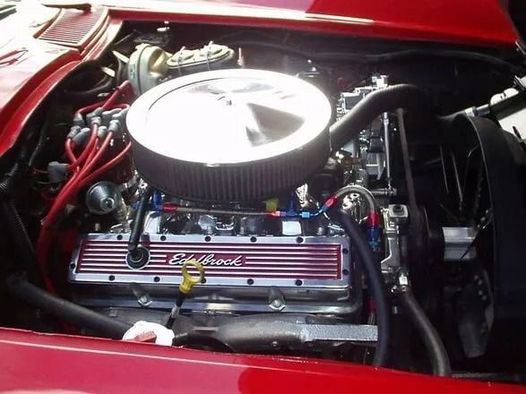 Car engine bay with a chrome air cleaner and red valve covers in a red-painted compartment