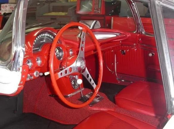 Red vintage car interior with red dashboard, steering wheel, and seats.