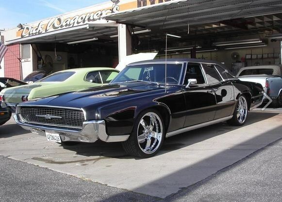 Black classic car parked outside a garage, with a green vintage car behind it