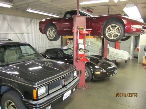 Cars in a workshop, with a red sports car raised on a lift above other vehicles.