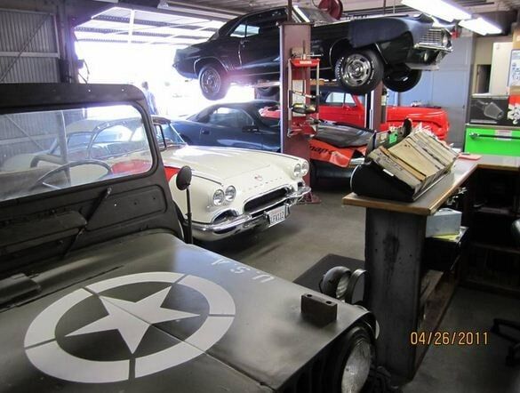 Car-filled garage with a gray Jeep in front, a white classic car, and a black car on a lift.